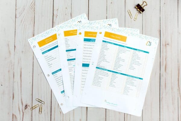 An overhead view of four organizing printables on a light wooden surface. The checklists are titled "School Supplies" and "College Checklist," with sections for various items. A black binder clip and a few gold paperclips are scattered around.