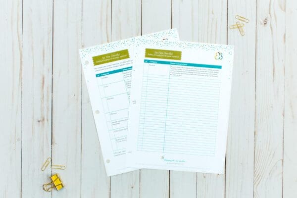 Two printed pages titled "Time-You Checklist" are placed on a white wooden surface. The organizing printable features sections for categories, activities, and notes. Nearby, there are a few paper clips and a yellow binder clip. The pages have colorful dotted borders.