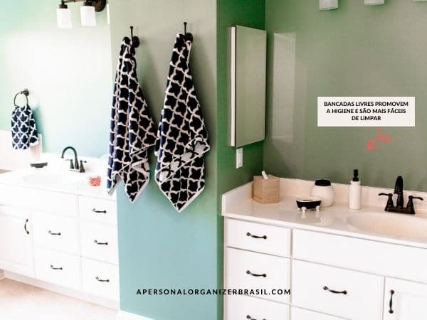 A bathroom with teal walls features white cabinets and countertops. Two dark-patterned towels hang on either side of a partition, while a red arrow points toward toiletries with text in Portuguese about cleanliness. An organizador para banheiro adds to the overall tidy aesthetic.
