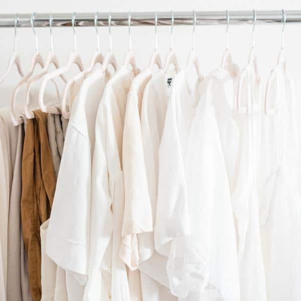 A clothing rack filled with neatly hung neutral-colored garments, including white, beige, and light brown shirts and blouses on identical hangers, demonstrates an impeccable method for organizing products. The softly blurred background enhances the clean and minimalist look.