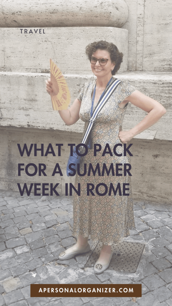 A woman in a floral dress holding a fan, standing on a cobblestone street in Rome, showing practical packing tips for staying cool during a summer trip.