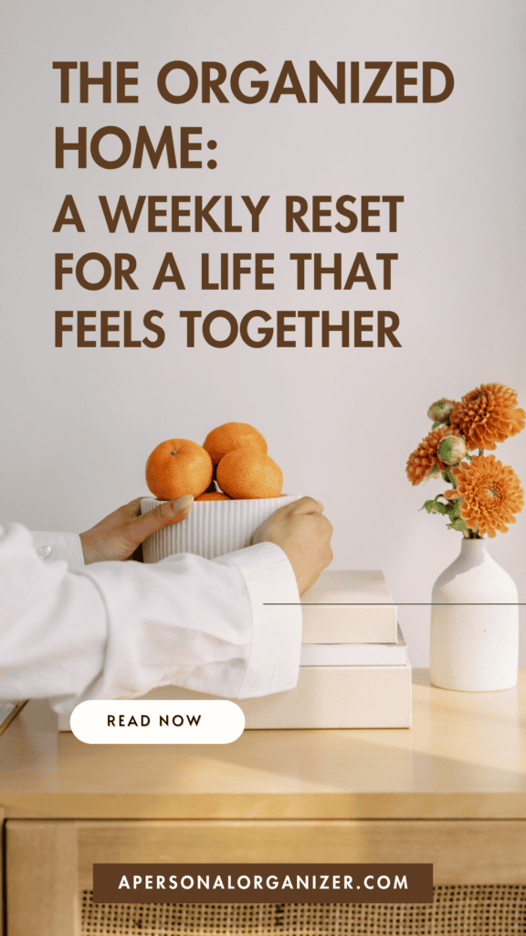 A person places a bowl of oranges on stacked books beside a vase with orange flowers, creating an inviting and organized home atmosphere. Text reads: “The Organized Home: A Weekly Reset for a Life That Feels Together.” Button says “Read Now.”.